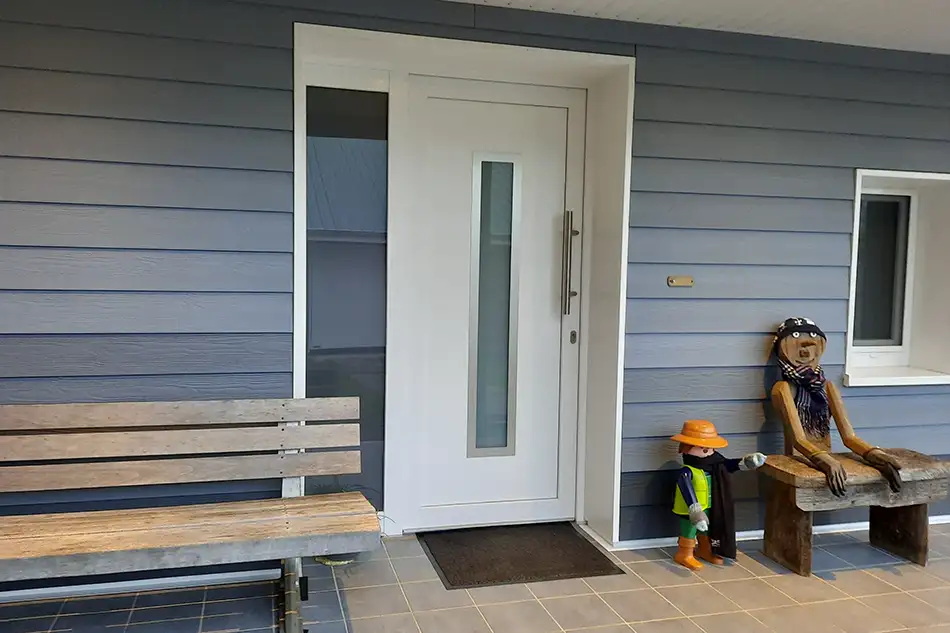Moderne weiße Kunststoff-Haustür mit Glasausschnitt und grauer Fassadenverkleidung, eingebaut von Tischlerei Heiko Hentschel Cuxhaven